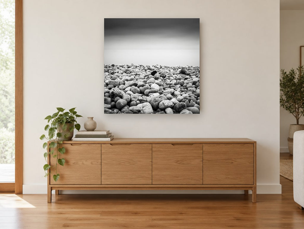 Pebble Shore Stillness coastal canvas print on the wall of a living room above a sideboard